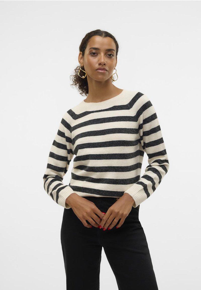 Gestreepte trui in crème en donkergrijs, met een ronde halslijn en lange mouwen met geribde manchetten. Model staat met de handen op de taille.