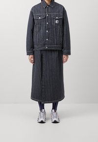 Jeansjack met bijpassende rok in donkerblauwe en witte verticale strepen. Vergezeld van witte sneakers met zwarte en gekleurde accenten.