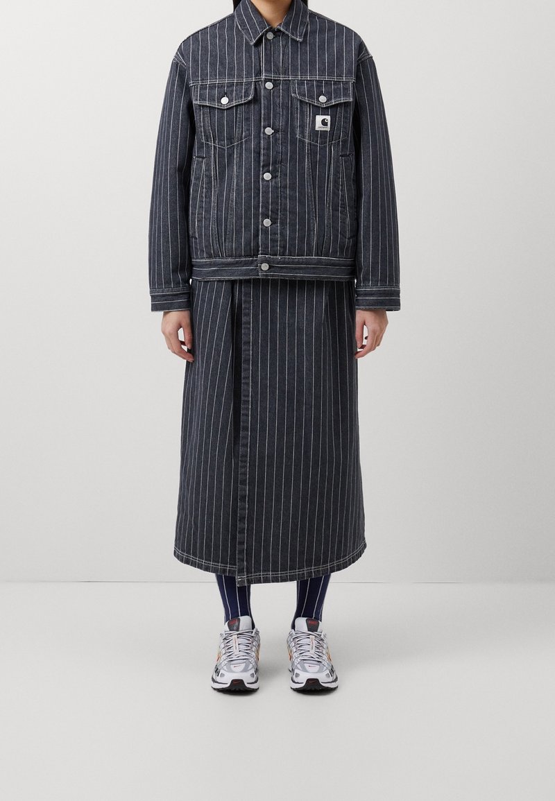Jeansjack met bijpassende rok in donkerblauwe en witte verticale strepen. Vergezeld van witte sneakers met zwarte en gekleurde accenten.