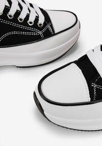 Baskets noir et blanc avec une tige en toile, bout rond, semelle épaisse blanche et coutures contrastées. Les lacets assurent le maintien de la silhouette.