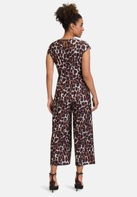 Leopardmuster-Overall aus einem seidig weichen Stoff, mit kurzen Ärmeln, weitem Bein und einem Keyhole-Detail im Rücken, kombiniert mit schwarzen High Heels.