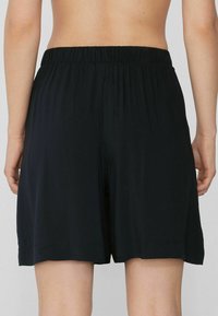 Pantalones cortos negros, ligeros, con una cintura elástica y un corte suelto. La tela tiene una textura suave y termina a mitad del muslo con un dobladillo simple.