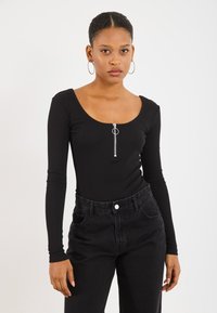 Zwarte longsleeve bodysuit met een ronde hals en zilveren ritssluiting. Gecombineerd met hoge zwarte denim jeans. Gladde stofstructuur.