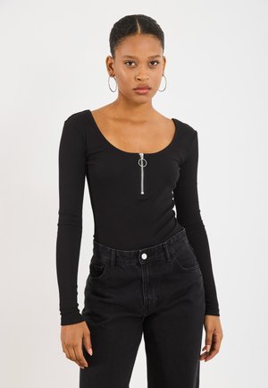 Black long-sleeve bodysuit with a scoop neckline and silver zipper detail. Paired with high-waisted black denim jeans. Smooth fabric texture.