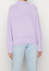 Pull à col roulé en tricot lavande avec poignets et ourlet côtelés, présentant un motif de point texturé. Associé à un denim bleu clair.