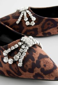 Leopardenmuster Ballerinas mit einer spitzen Zehe, die vorne mit funkelnden Kristallverzierungen versehen sind. Glattes Material und detaillierte Akzente.
