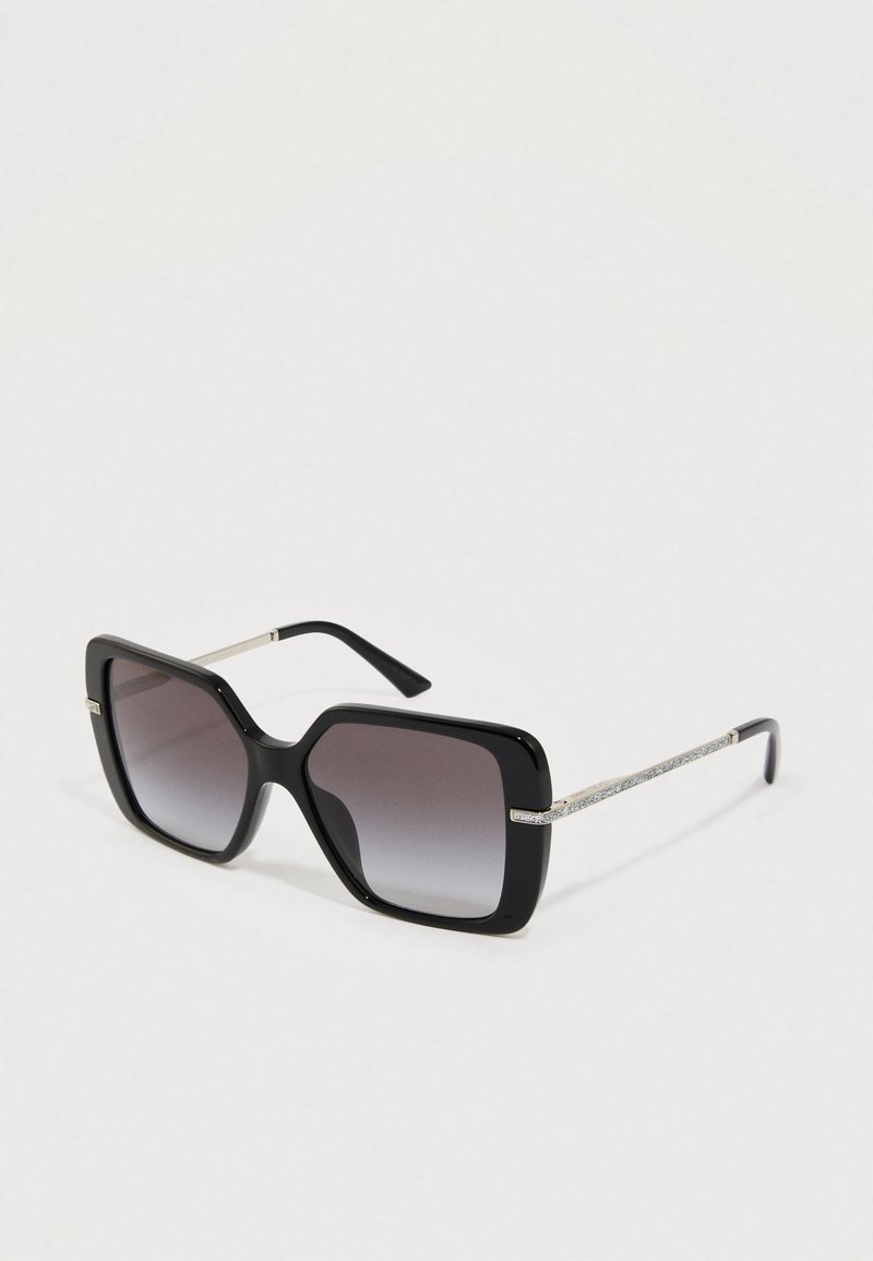 Sorte oversize solbriller med gradient grå linser, en tyk plastikramme og metalstel med en dekorativ glitrende detalje.