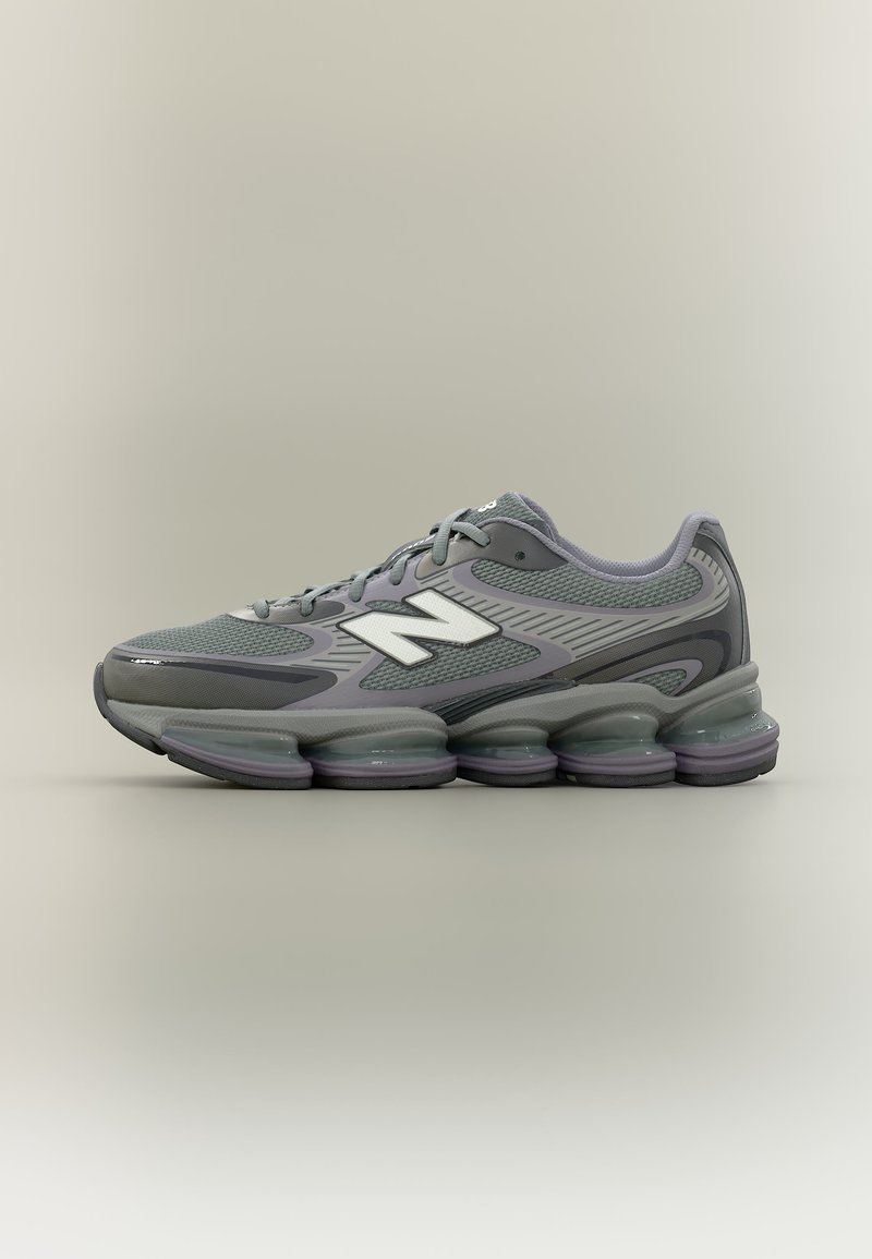 Γκρι και μαύρο αθλητικό παπούτσι New Balance με λευκό λογότυπο, πλέγμα πάνω μέρος και επενδεδυμένη τμηματική σόλα, εμφανιζόμενο σε πλάγια όψη.