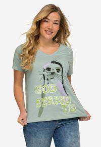 Camiseta de cuello v en verde claro con un gráfico de un animal de dibujos animados y el texto "GOD STRANDTID" en tipografías negritas y juguetonas. Tejido suave, corte relajado.