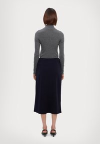 Gray ribbed turtleneck top paired with a dark navy, smooth, mid-length skirt. Black heeled sandals with small buckles complete the outfit.