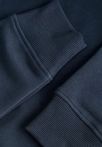 Manches de sweat-shirt bleu marine foncé avec poignets côtelés qui se chevauchent sur une surface plane montrant la texture du tissu et les détails de la couture.