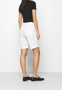 Shorts bianchi in cotone con risvolti, dotati di due tasche posteriori, abbinati a un top nero aderente e mocassini neri. Design semplice e casual.