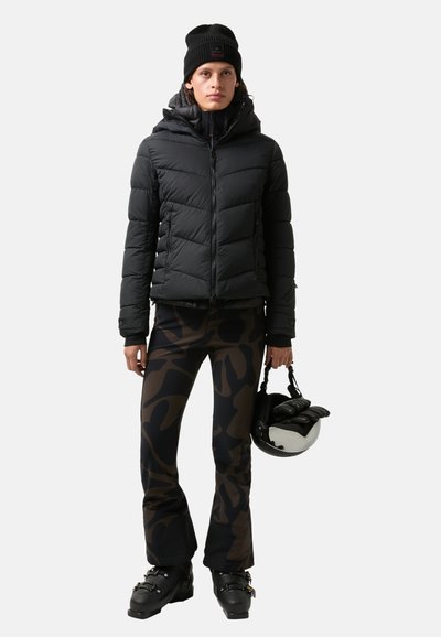 Czarna kurtka puchowa z pikowanym wzorem i kapturem, zestawiona z brązowymi spodniami w kamuflażu. Dodatki to czarna dzianinowa czapka i kask.