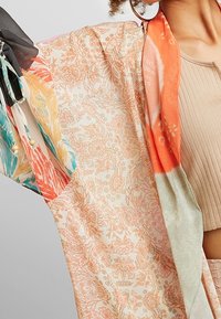 Lehký kimono s květinovým vzorem v jemných oranžových a krémových tónech, s živými akcenty v tyrkysové a korálové barvě na rukávech.