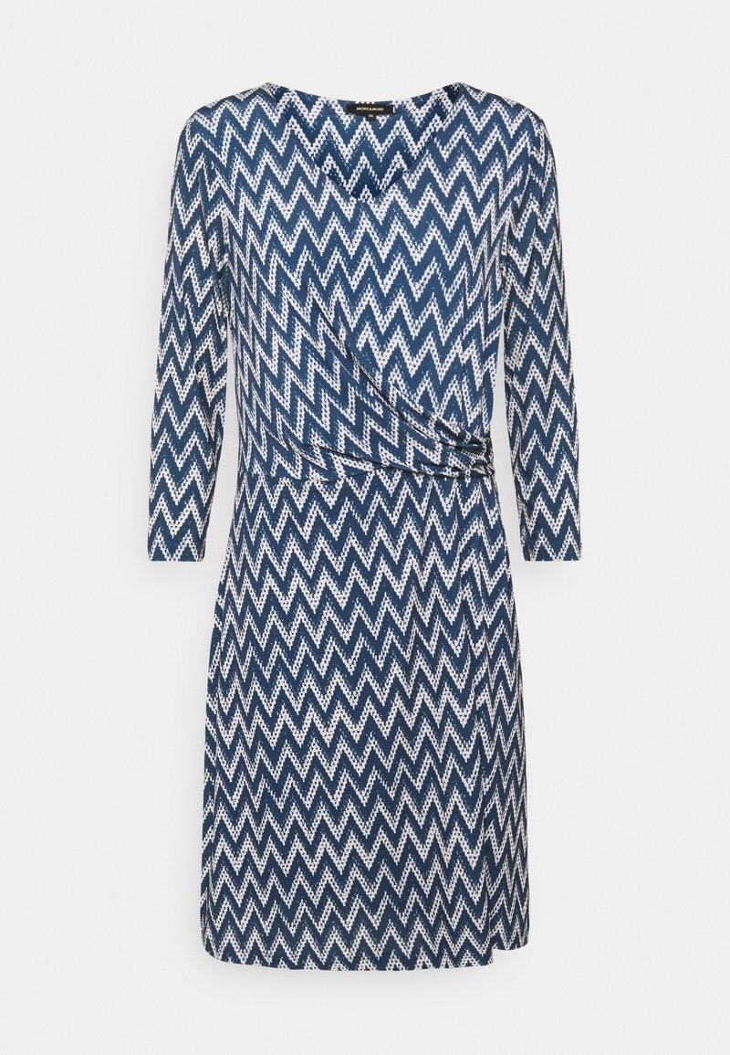 Mörkblå klänning med vit zigzag-mönster, omslagdesign, långa ärmar och med cinchad midja. Mjuk, texturerad tyg.