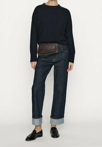 Marinblå oversized tröja, mörk denimjeans som är uppvikta vid fållarna, och svarta loafers. Bananväska i brunt läder med klaffstängning.