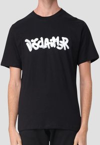 Persona che indossa una maglietta nera a maniche corte con la parola "Disclaimer" in testo bianco stile graffiti sulla parte anteriore.