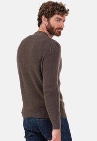 Pull marron côtelé en tissu texturé, doté d'un col rond et de manches longues, associé à un jean en denim foncé.