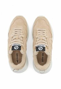 Beige suede sneakers with plush lining, featuring rounded toe, textured upper, flat laces, and logo tag. White rubber sole.