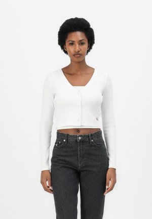 Witte cropped cardigan met een V-hals en knoopsluiting, gecombineerd met hooggetailleerde donkere jeans. Gebreide textuur met lange mouwen.