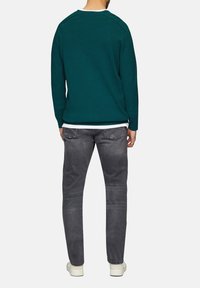 Türkiser Pullover mit Rundhalsausschnitt und langen Ärmeln, kombiniert mit schmal geschnittenen grauen Jeans und weißen Turnschuhen, von hinten betrachtet.