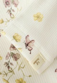 Bloemmotiefstof in zachte tinten van geel en roze, met een vlinder en een label met de tekst "Lil' Atelier."