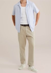 Ljusblå randig skjorta med kort ärm över en vit linne, kombinerad med beige byxor och vita sneakers, med ett svart bälte.