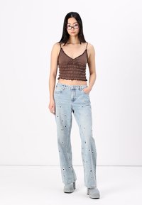 Brun ruchet crop top og lyseblå vide bukser med flere blomsterbroderi detaljer. Modellen har på seg platåsko.
