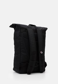 Sac à dos noir à rabat avec des sangles rembourrées ajustables, en tissu durable, et un détail de logo. Possède un dos texturé pour le confort et le soutien.