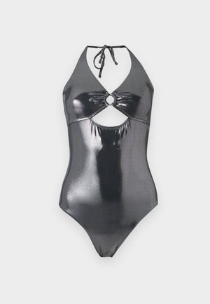 Jeune femme debout pieds nus portant un maillot de bain une-pièce métallique foncé et brillant avec un col halter et une découpe sur le devant.