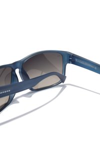 Siniset puoliläpäisevät aurinkolasit harmailla liukuvärilinssillä. Sankojen pinta on mattapintainen ja siellä on hillitty brändäys sivulla. Kevyt muotoilu.
