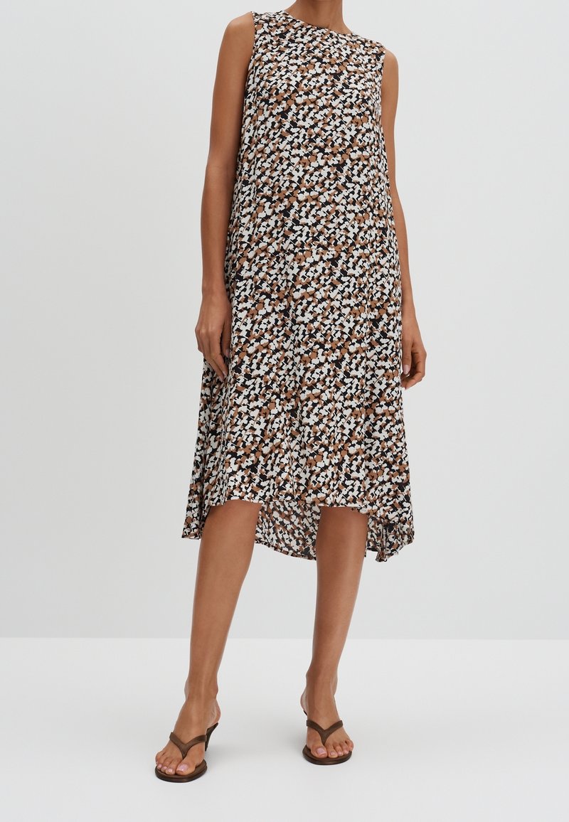 Ærmeløs kjole i et brunt, hvidt og sort blomstermønster, knælængde med en asymmetrisk kant. Letvægtsstof, flydende design.