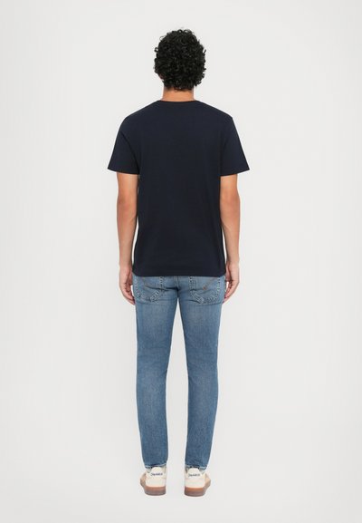 Navy blue cotton T-shirt with short sleeves and crew neckline, paired with light blue denim jeans and tan casual shoes. Simple and functional look.