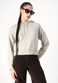 Világosszürke, cropped fazonú kapucnis pulóver, texturált kötött anyagból, húzózsinórral ellátott kapucnival és bordás szegéllyel, sötétbarna kordbársony nadrággal párosítva.