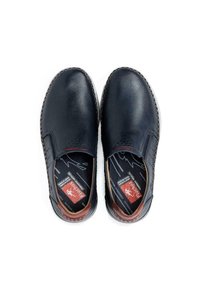 Zapatos de piel azul marino tipo slip-on con un diseño perforado, acentos marrones contrastantes y una suela texturizada. El interior muestra etiquetas de marca.