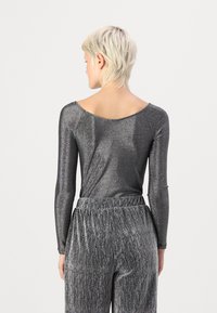 En metallisk grå langermet bodysuit med bred utringning og en jevn, blank tekstur, kombinert med matchende plisserte bukser.