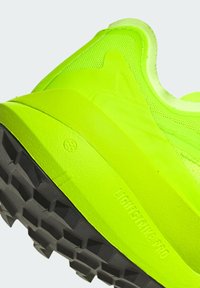 La scarpa da ginnastica di un brillante giallo neon presenta una tomaia testurizzata, una suola intermedia liscia e una suola esterna in gomma nera con un distintivo motivo di battistrada.