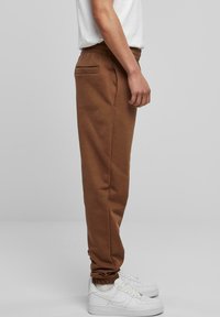 Bruine sweatpants van zacht materiaal, met een elastische tailleband en zijzakken. Gecombineerd met witte sneakers voor contrast.
