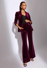 Plüss, mély bordó bársony blézer és megegyező flare nadrág, fekete toppal és fekete pántos szandállal párosítva. Finom fény mindenhol.