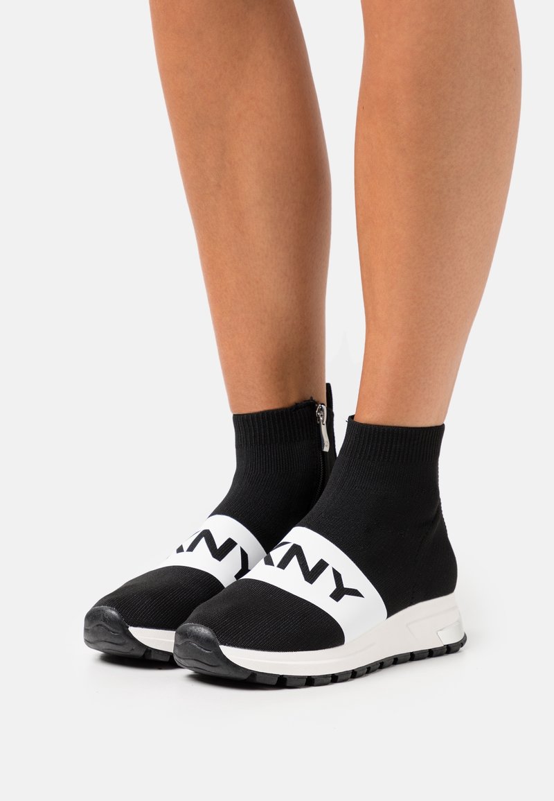 Czarne sneakersy w stylu skarpetkowym z białym paskiem oznaczonym napisem "DKNY", zapięciem na zamek, teksturowanym materiałem i sportową gumową podeszwą.