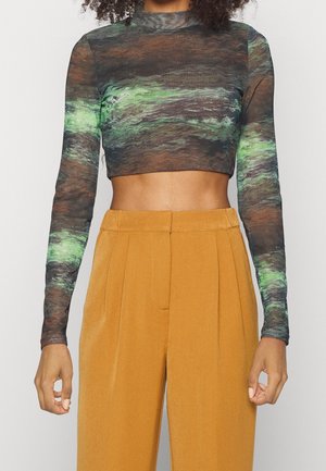 Top corto de mangas largas con un patrón en espiral multicolor en verde, marrón y negro. Combinado con pantalones de talle alto color mostaza.