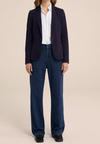Marinblå blazer med en enda knapp, kombinerad med högmidjade, vida mörk denimjeans och svarta läderskor, vilket skapar en skräddarsydd look.