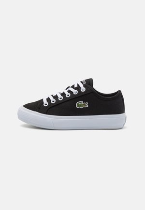 Czarny niski materiałowy sneaker z białymi sznurowadłami, białą podeszwą i zielonym logo krokodyla po boku.
