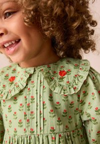 Das grüne Blumenmuster-Kleid verfügt über einen rüschengesäumten Kragen mit roten und grünen Blumenmustern. Hergestellt aus weichem Stoff, hat es eine geraffte Taille und Falten.