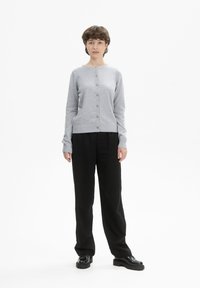 Hellgrauer Strickcardigan mit Rundhalsausschnitt, Knopfverschluss und gerippten Bündchen, kombiniert mit lockeren schwarzen Hosen und dunklen Schuhen.