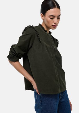 Chemise en velours côtelé vert olive avec des accents froncés le long du col et des épaules ; manches longues avec des poignets retroussés.