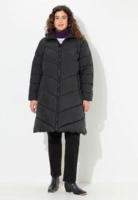 Svart puffjacka med chevronstickning, dragkedjestängning och sidofickor. Bärs över mörka byxor och ankelskor, med hög krage.