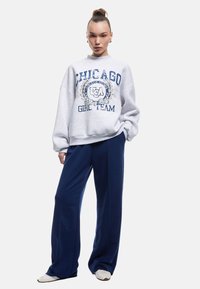 Grå oversized sweatshirt med "CHICAGO" og "GIRL TEAM" trykt i marineblå. Kombineret med løse marineblå bukser og hvide sneakers.