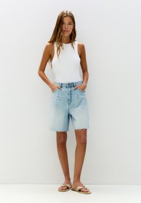 Shorts en denim bleu clair avec bords effilochés, taille haute et deux poches avant, associés à un top sans manches blanc et des sandales embellies.