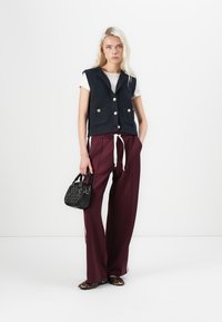 Marineblauw geribbelde gebreide vest met gouden knopen, witte t-shirt, bordeaux brede broek en zwarte handtas. Schoenen met luipaardprint.